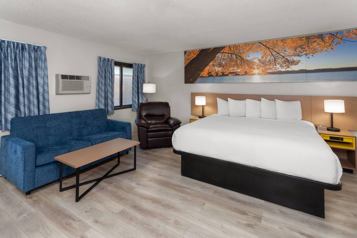 Une chambre d’hôtel avec un grand lit, un canapé bleu, un fauteuil en cuir marron et une table en bois.