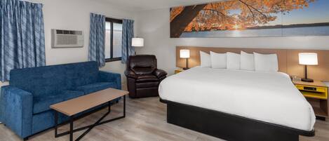 A hotel room with a large bed, a blue sofa, a brown leather chair, and a wooden table.