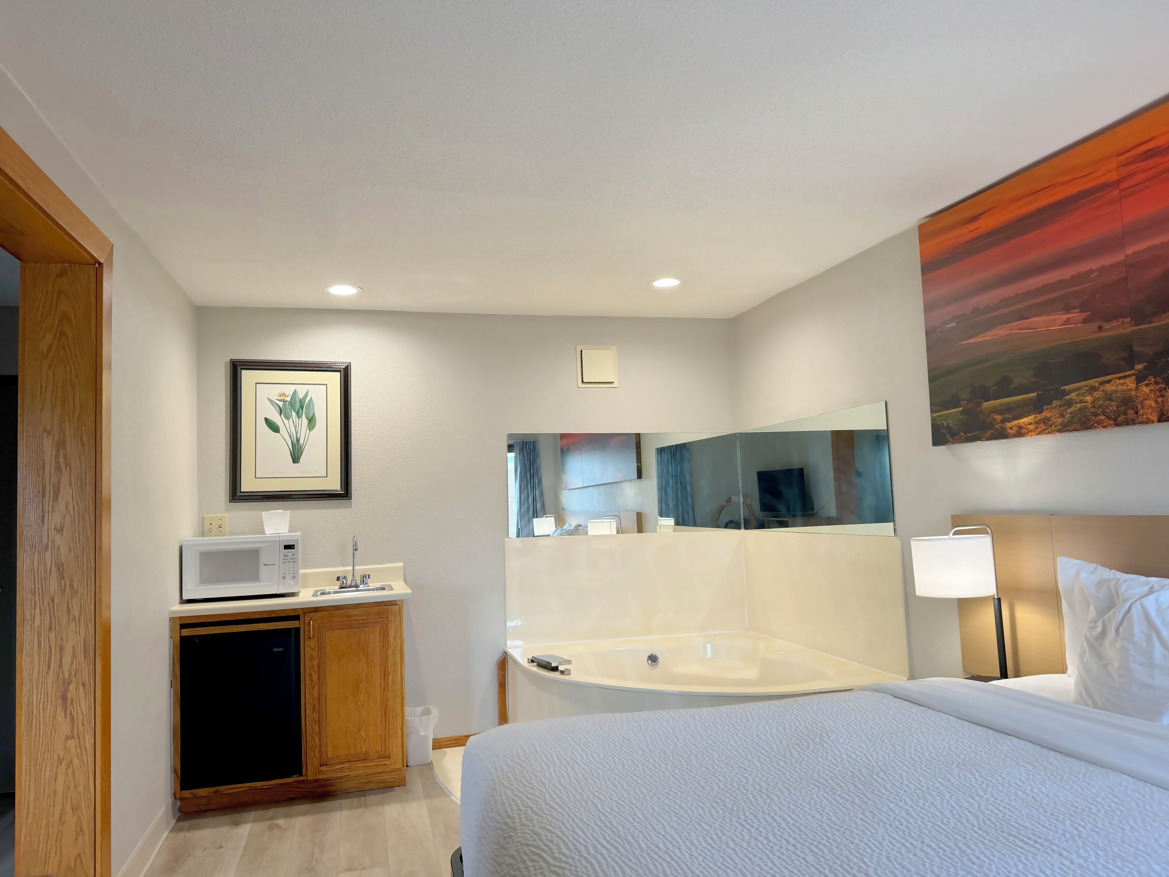 Ein Hotelzimmer mit Bett, Spüle, Mikrowelle, Schrank, Spiegel und einem Bild an der Wand.