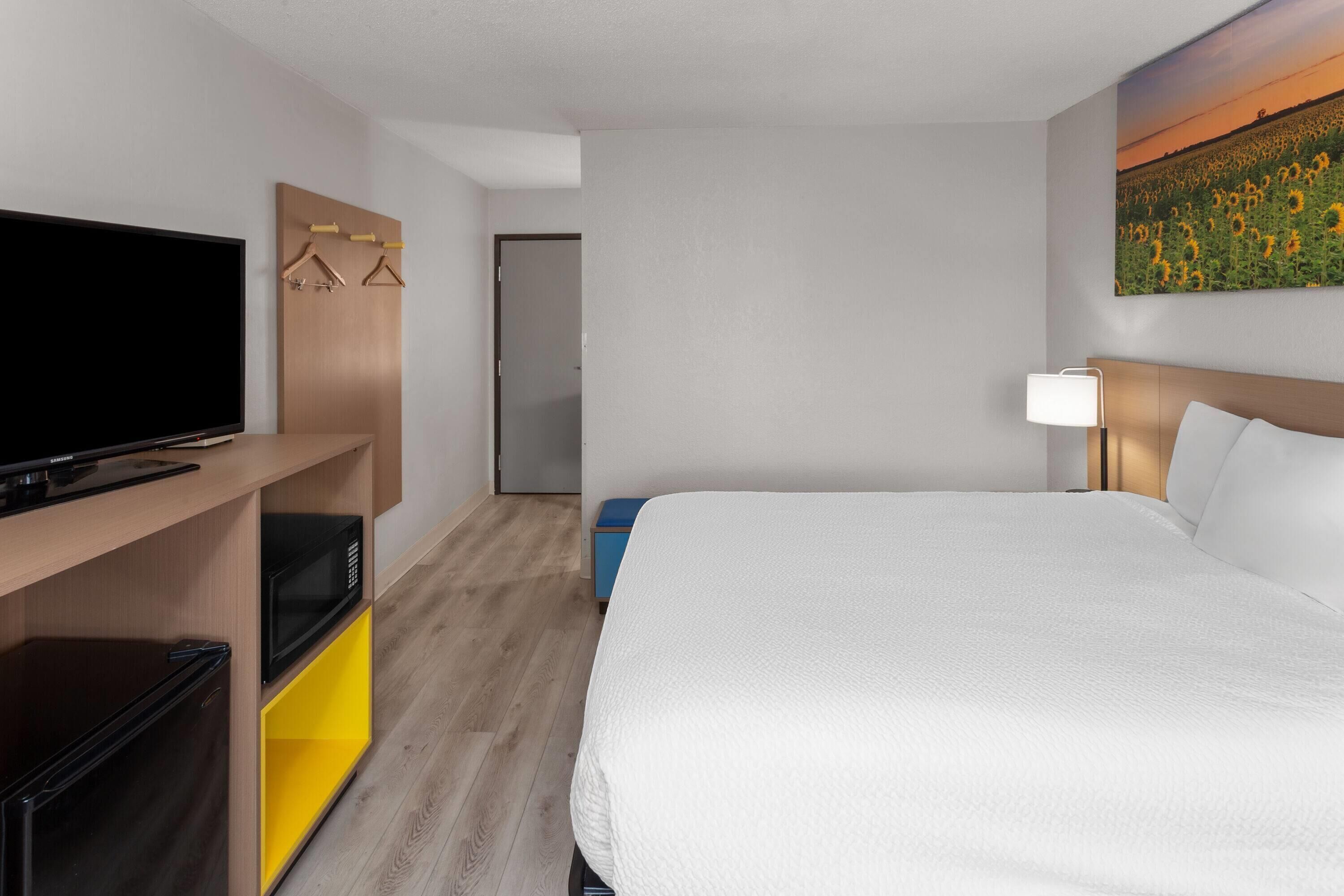 Una habitación de hotel con una cama grande, un televisor de pantalla plana, un microondas y un escritorio pequeño con lámpara.