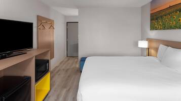Una habitación de hotel con una cama grande, un televisor de pantalla plana, un microondas y un escritorio pequeño con lámpara.
