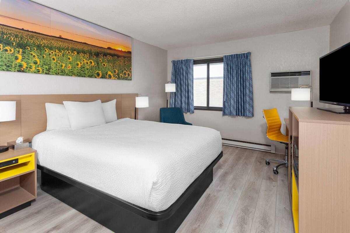 Une chambre d’hôtel avec un grand lit, un bureau avec une chaise, une télévision et une fenêtre avec des rideaux.