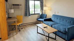 A hotel room with a wooden desk, a blue sofa, a yellow chair, and a window with curtains. - Days Inn by Wyndham Mason City (Mason City)