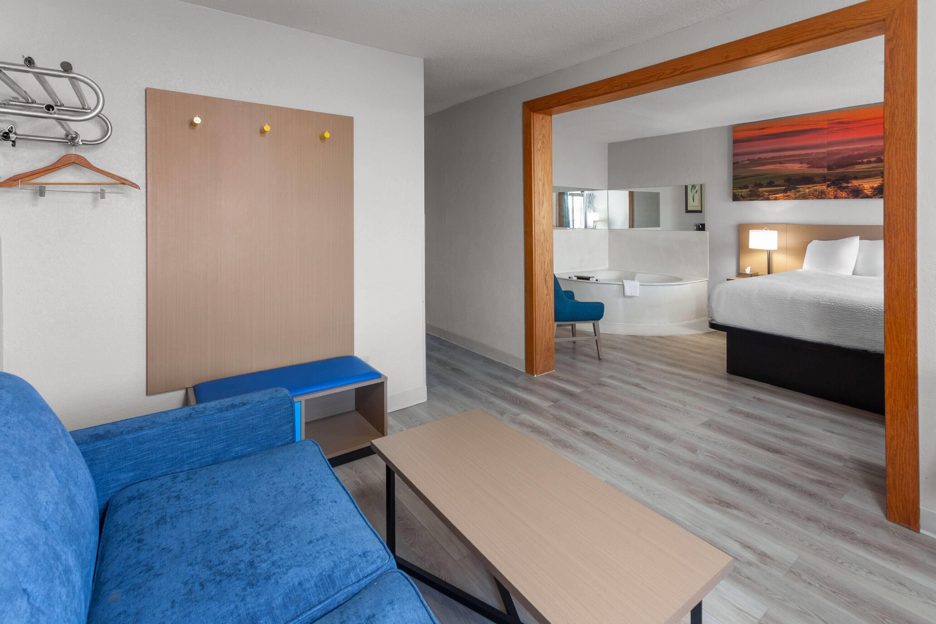 Une chambre d’hôtel avec un lit, un bureau, une chaise, un porte-manteau et une porte en bois.