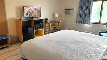 Quarto de hotel com uma cama grande, televisão em uma prateleira de madeira, escrivaninha com cadeira, micro-ondas e ar condicionado.