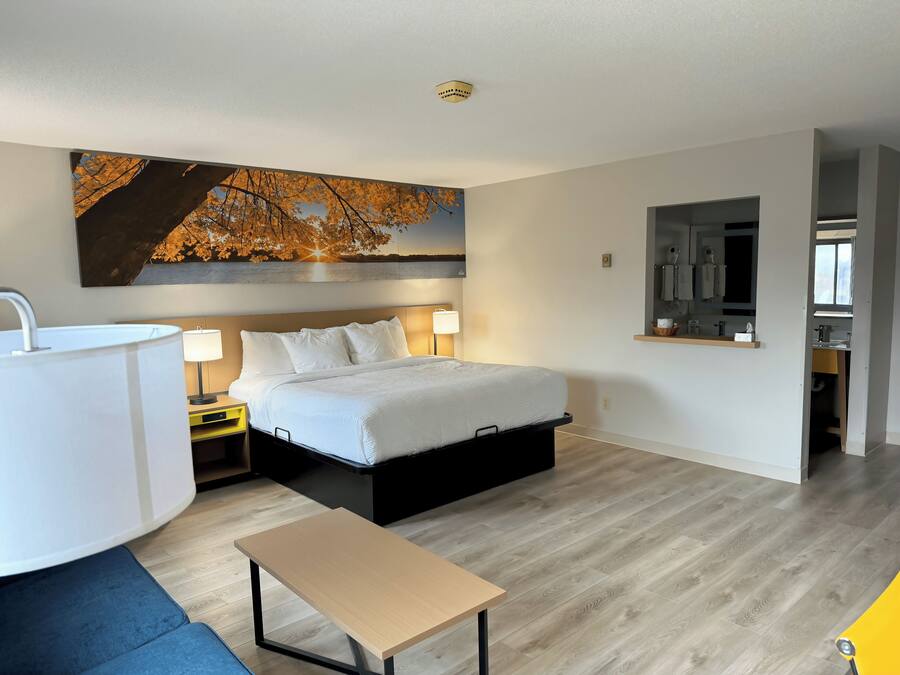 Ein modernes Schlafzimmer mit einem großen Bett, Nachttischen, einem Schreibtisch und einem durch eine offene Tür einsehbaren Badezimmer.