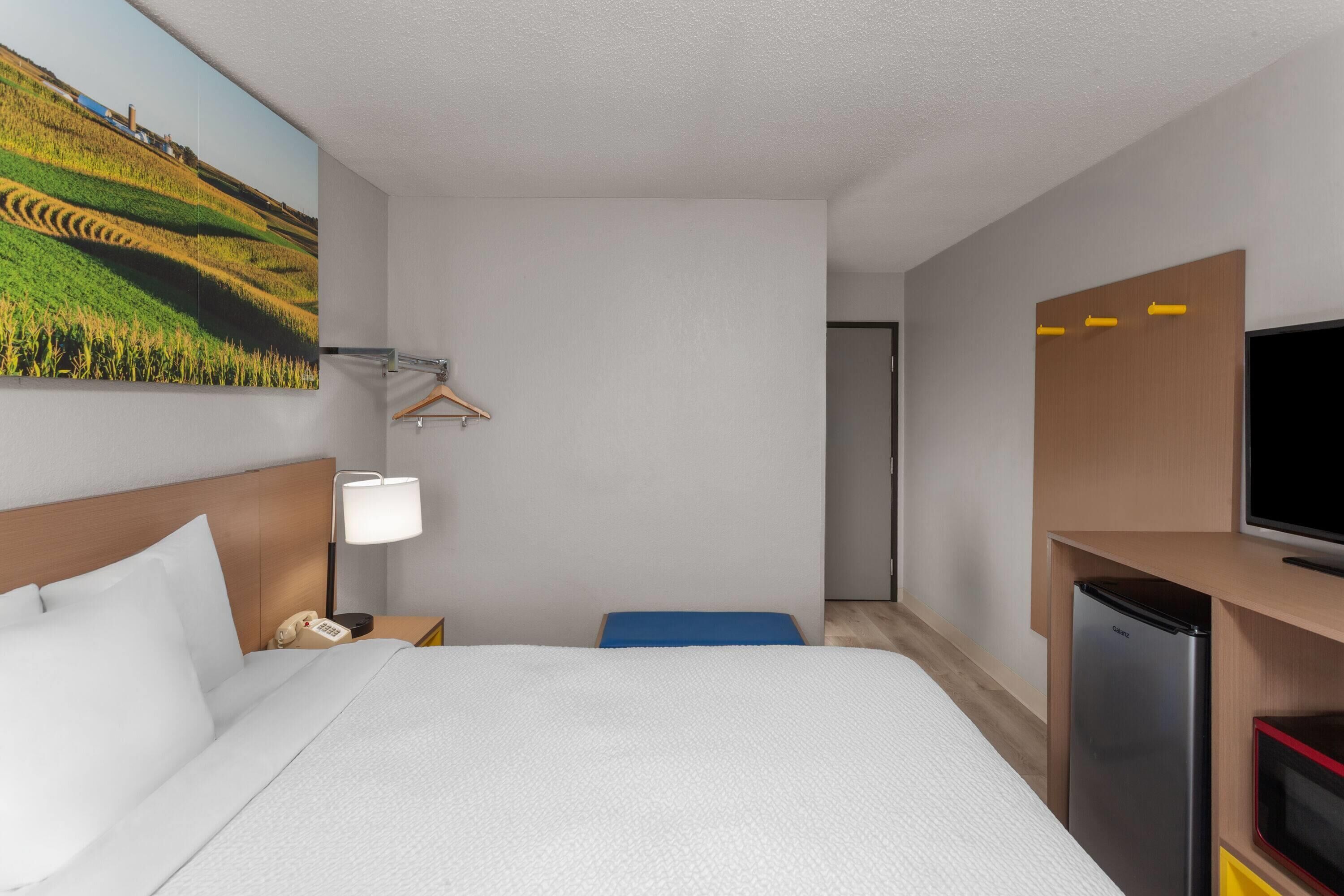 Une chambre d’hôtel équipée d’un lit, d’un bureau avec une lampe, d’une télévision et d’un réfrigérateur.