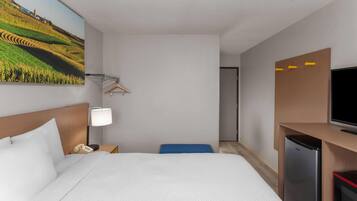 Une chambre d’hôtel équipée d’un lit, d’un bureau avec une lampe, d’une télévision et d’un réfrigérateur.
