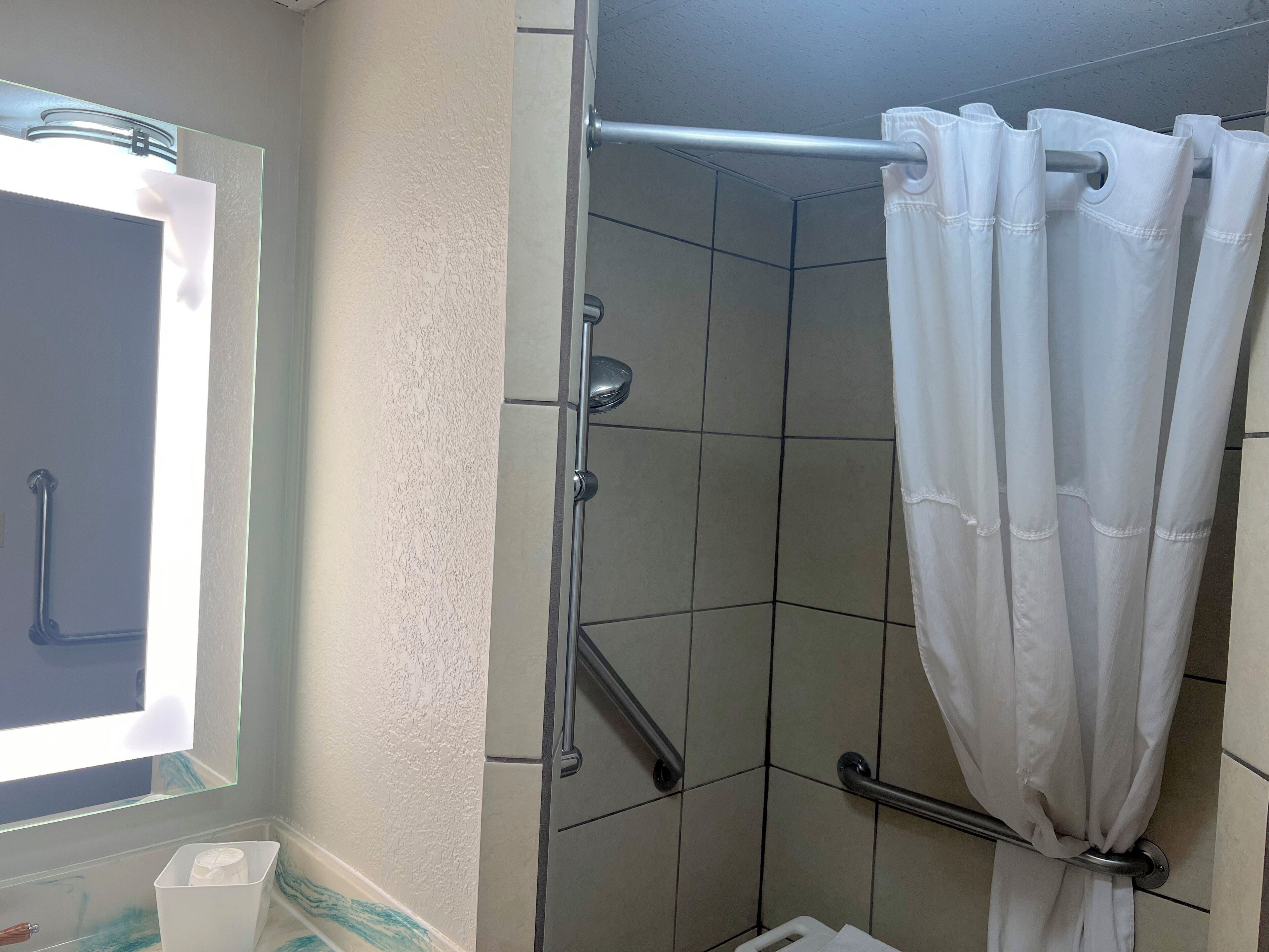 A shower area with a white curtain, a handrail, and a tiled wall.