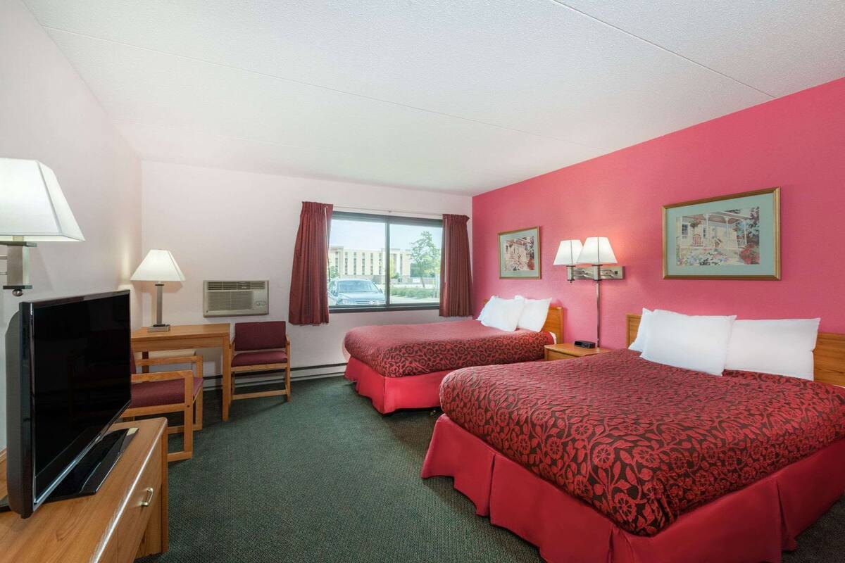 Une chambre d’hôtel avec deux lits, une télévision, un bureau et une fenêtre avec des rideaux.