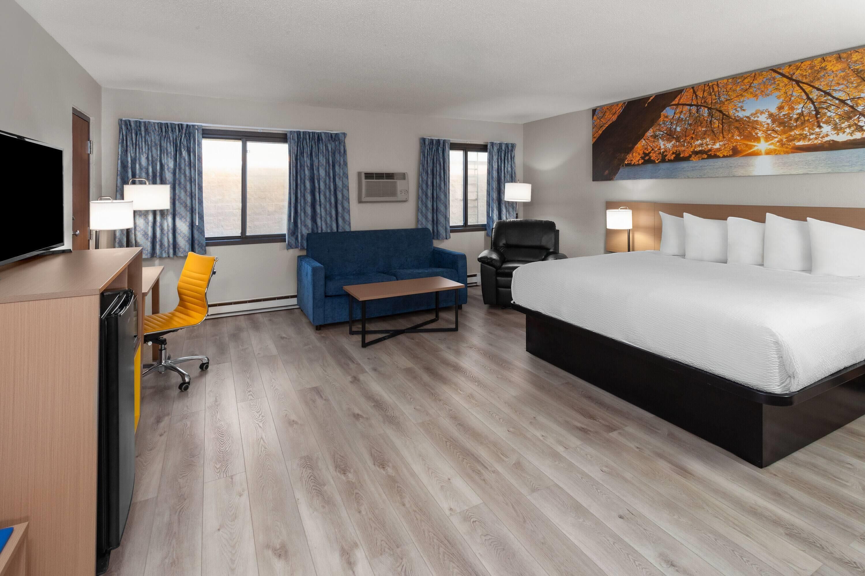 Una habitación de hotel con una cama, un escritorio con televisor, un sofá y una silla.