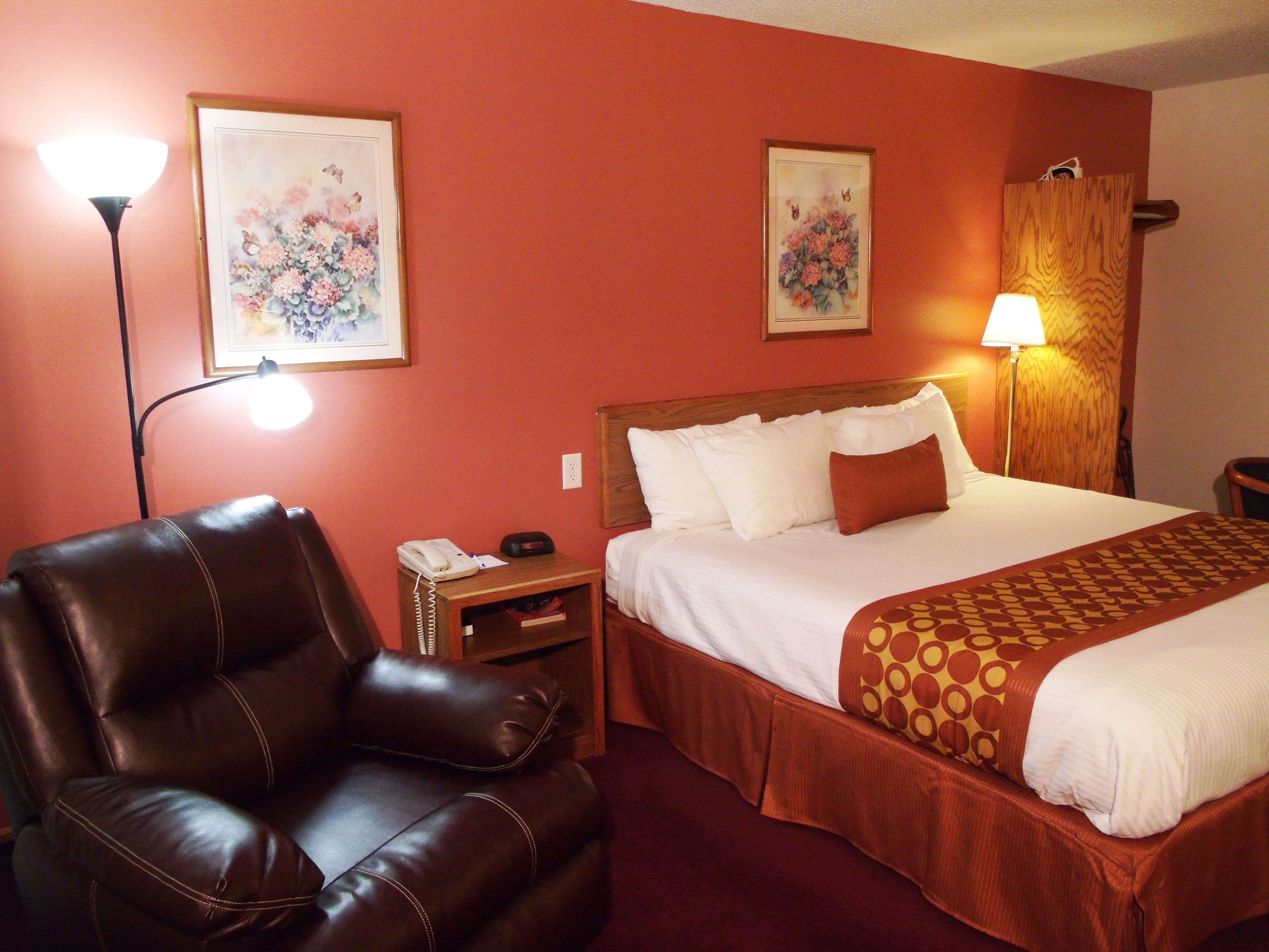 A hotel room with a bed, a leather chair, a nightstand with a phone, and two wall-mounted lamps.