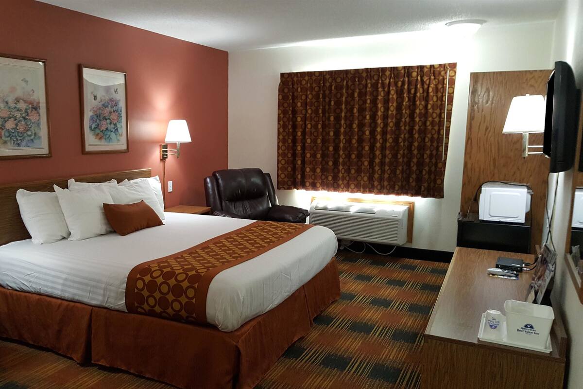 A hotel room with a large bed, a desk, a chair, an air conditioning unit, and a television.