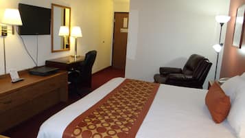 A hotel room with a bed, desk, chair, TV, and lamps.