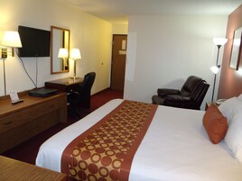 Habitación de hotel con cama, escritorio, silla, televisor y lámparas.