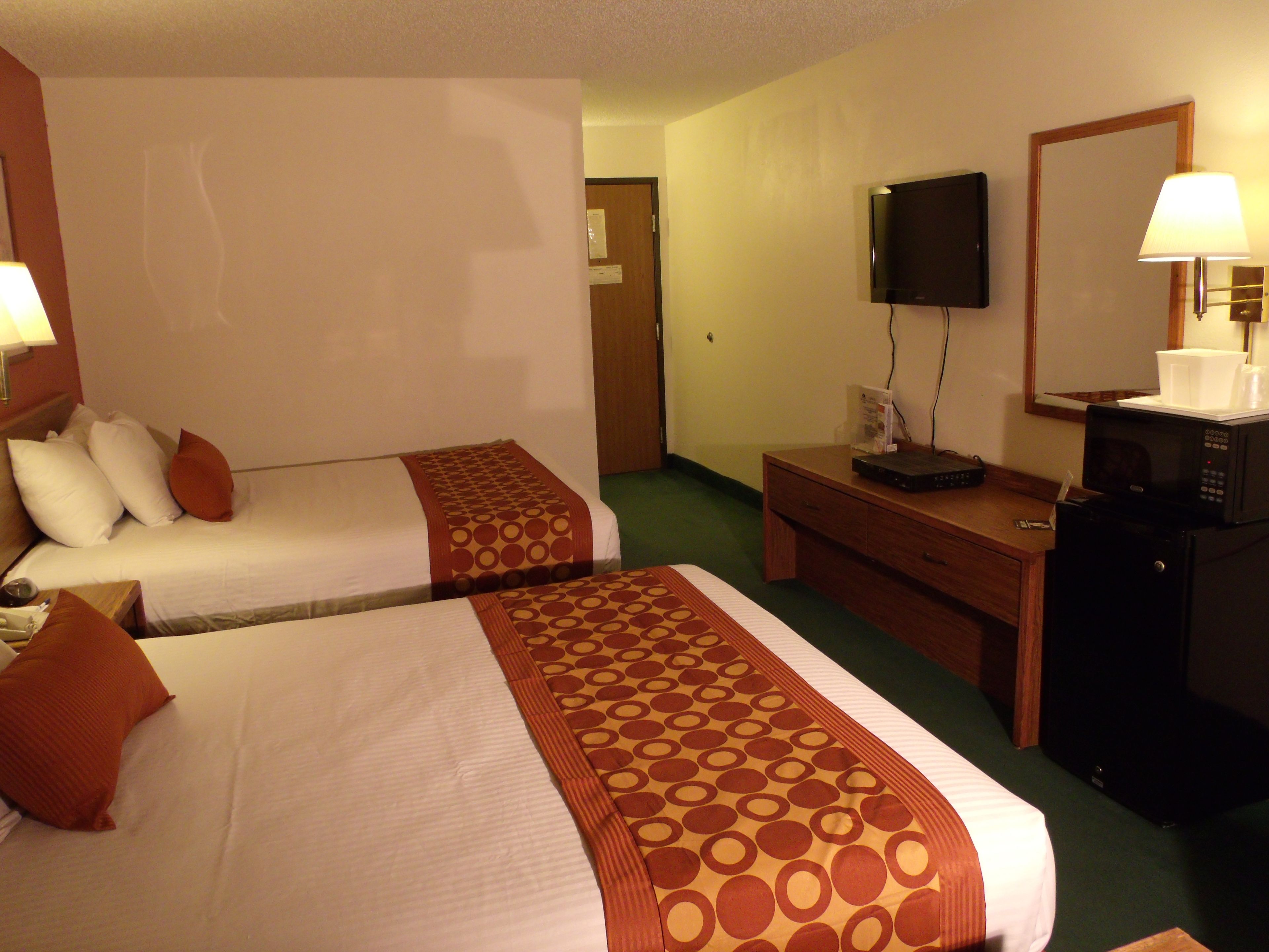 A hotel room with two beds, a desk, a television, and a microwave.