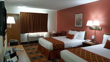 A hotel room with two beds, a desk with a computer, a window with curtains, an air conditioner, and a painting on the wall.