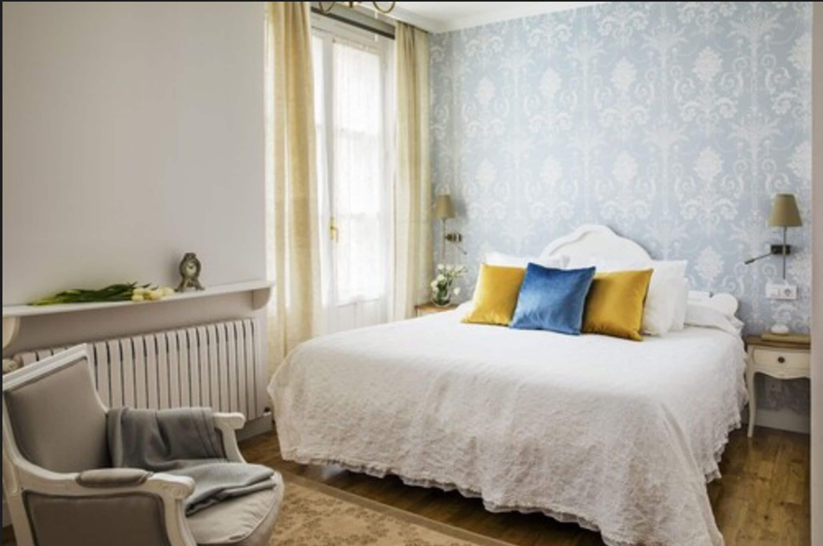 A bedroom with a large bed, a chair, a radiator, and a window with curtains.