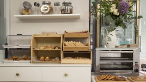 Una vitrina de panadería con pasteles, una máquina de café y un jarrón con flores.