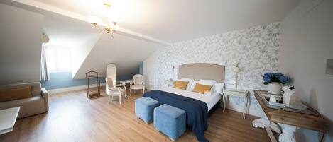 A bedroom with a bed, two ottomans, a desk, a chair, and a lamp.