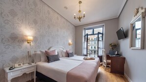 Habitación de hotel con dos camas, un escritorio con computadora, televisor montado en la pared y ventana con vista a edificios.