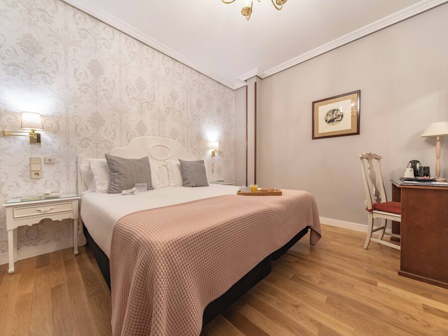 Un dormitorio ordenado con cama, mesitas de noche, un escritorio y una silla.