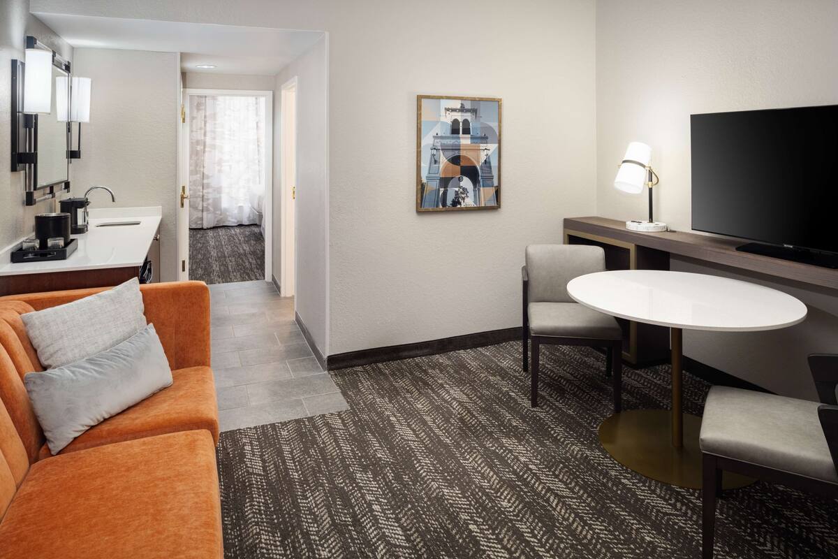 Hotelkamer met een bank, een klein tafeltje met een lamp, een televisie en een schilderij aan de muur.