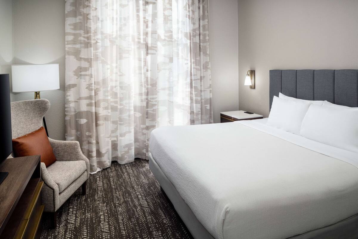 Een hotelkamer met een groot bed, een stoel, een bureau en een lamp.
