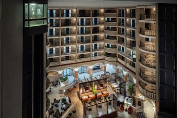 A modern building with a glass facade and a large overhang, surrounded by palm trees and other buildings. at Embassy Suites by Hilton Orlando North