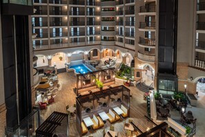 Un vestíbulo de hotel de varios niveles con piscina, zonas de estar y restaurante.