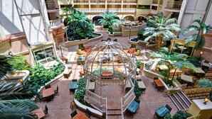 Un vestíbulo de hotel con varios niveles, zonas de estar al aire libre y un jardín central.