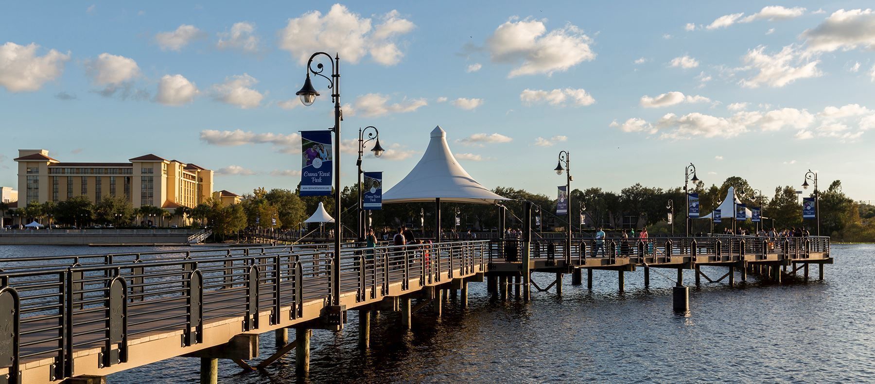 A waterfront promenade with a covered pavilion, a bridge, and a hotel in the background.