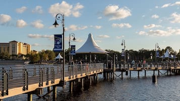 A waterfront promenade with a covered pavilion, a bridge, and a hotel in the background.
