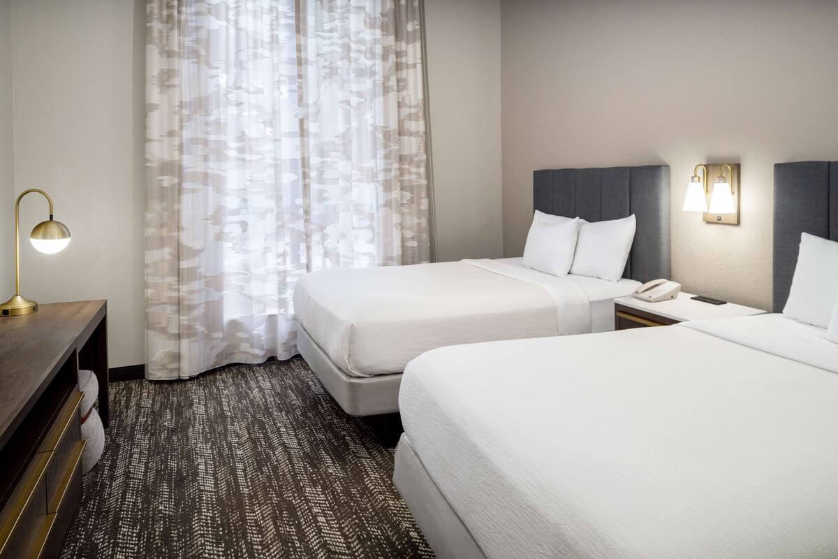 Een hotelkamer met twee bedden, een bureau, een lamp en een telefoon.