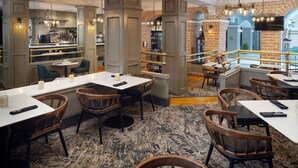 Un restaurante con varias mesas y sillas, una zona de bar y vistas a la ciudad a través de grandes ventanales.