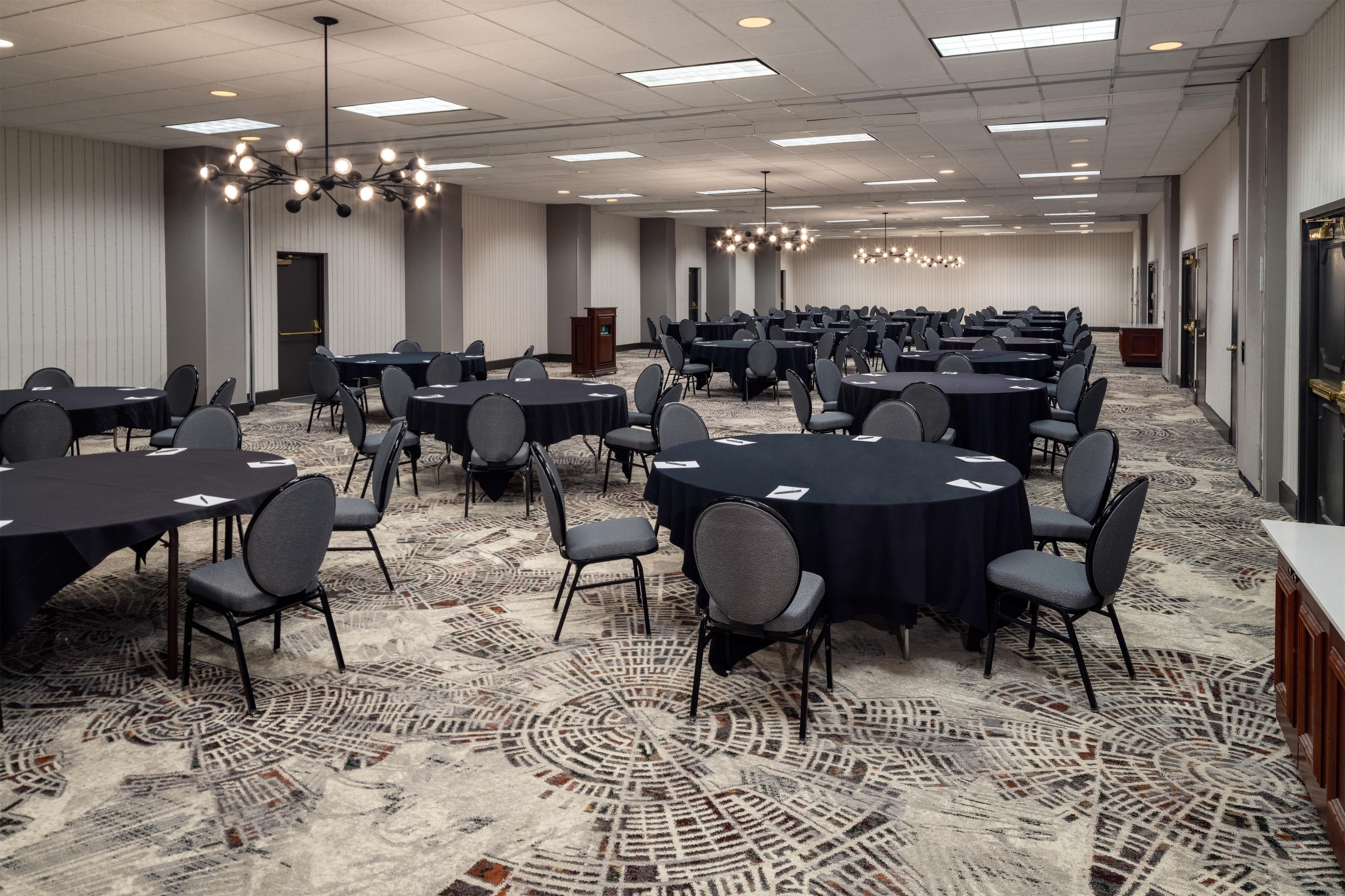 A conference room with multiple tables and chairs, a patterned carpet, and a ceiling with recessed lighting.