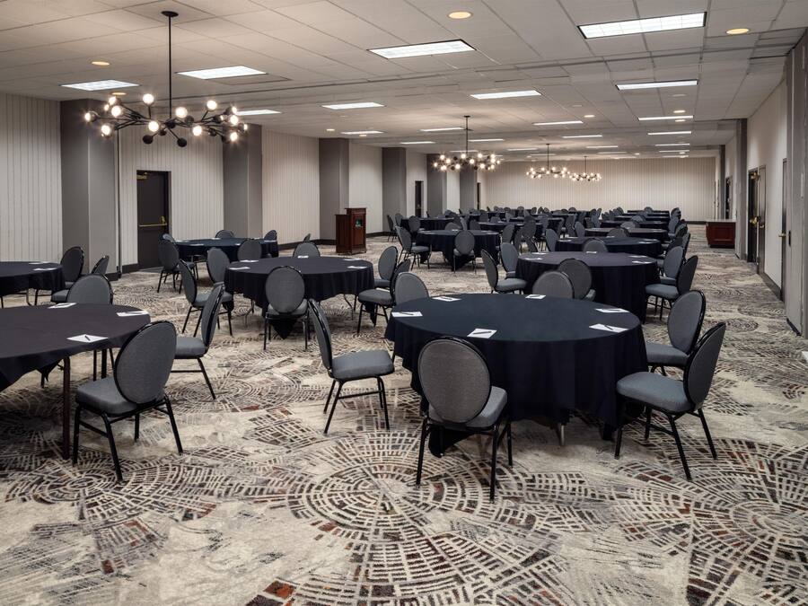 Un salón de conferencias con varias mesas y sillas, una alfombra estampada e iluminación empotrada en el techo.