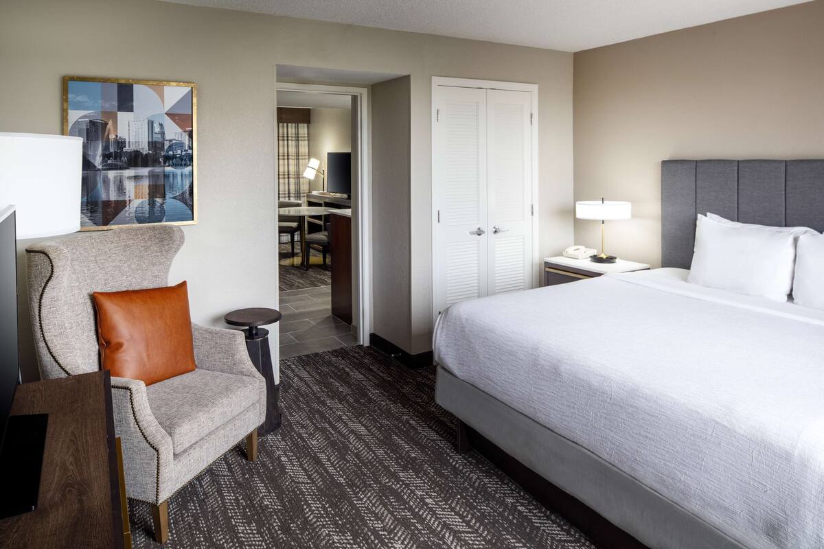 Hotelkamer met een groot bed, een stoel, een bureau en een stadsgezichtschilderij aan de muur.