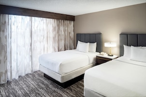 Habitación de hotel con dos camas, una mesita de noche con lámpara y un ventanal con cortinas.