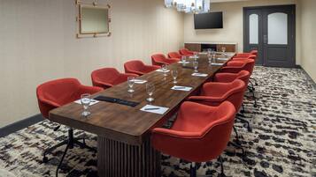 A conference room with a long table, red chairs, and a television on the wall.