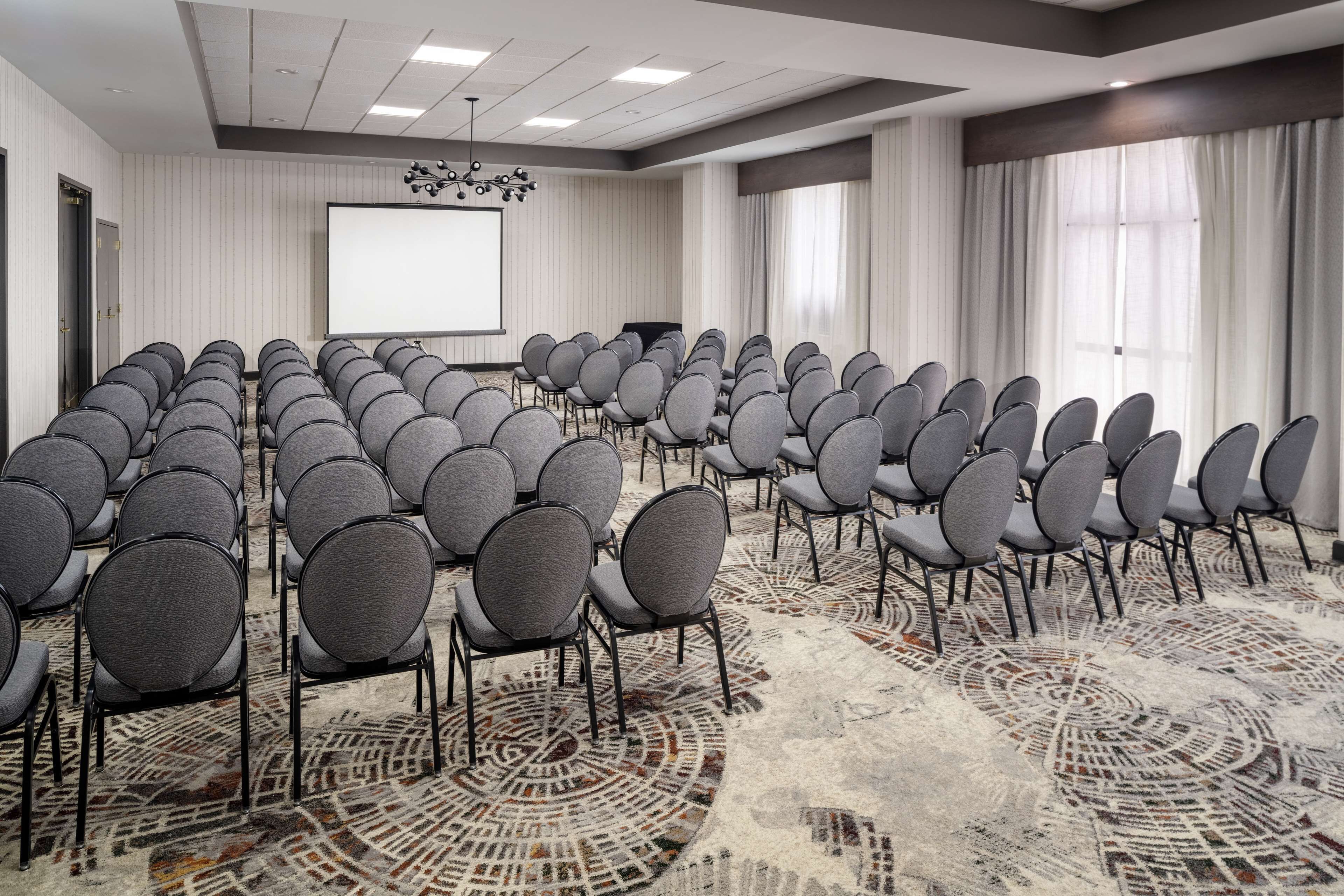 A conference room with rows of grey chairs, a large screen, and a patterned carpet.