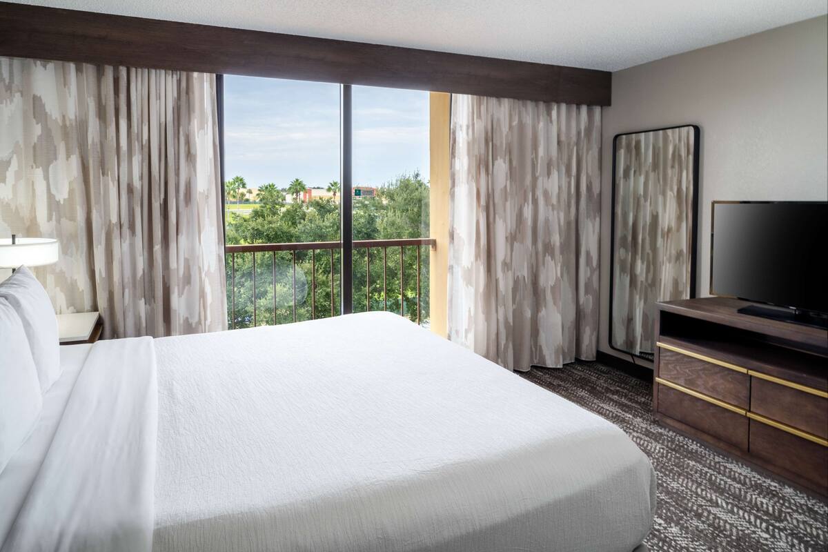 Een hotelkamer met een groot bed, een televisie en uitzicht op groen buiten het raam.