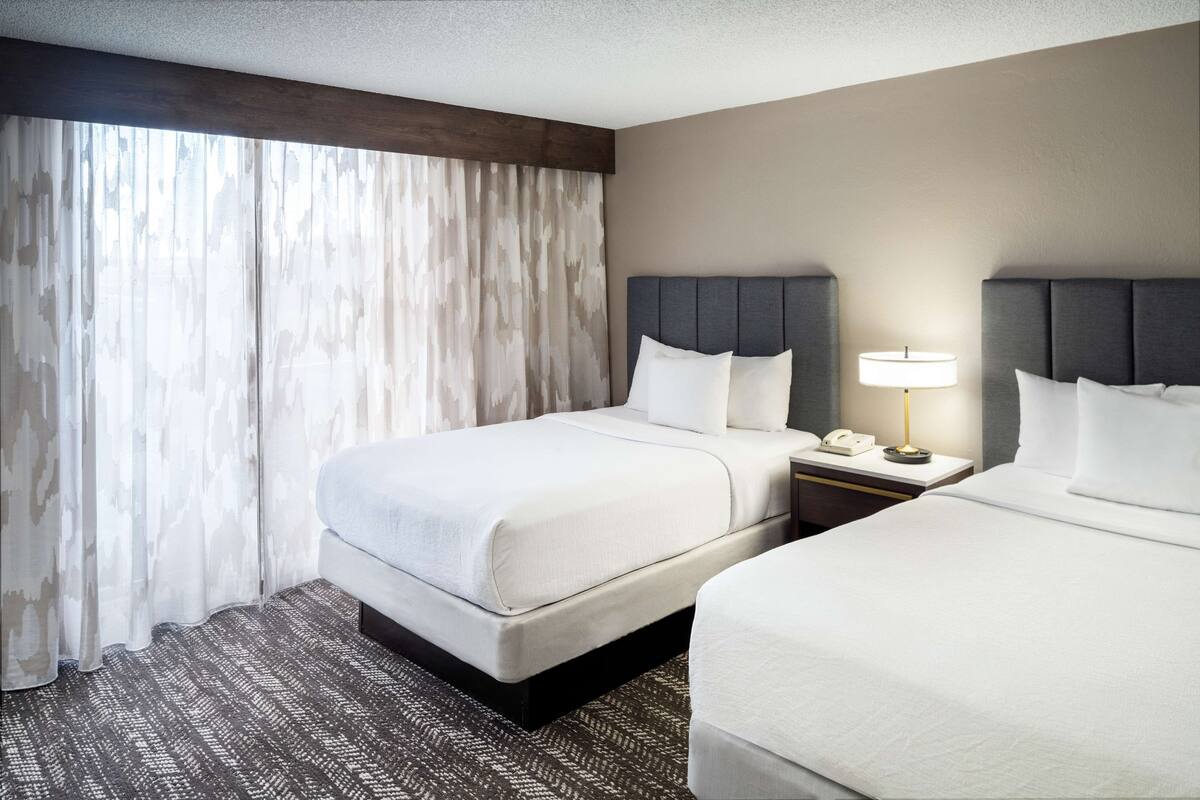 Een hotelkamer met twee bedden, een nachtkastje met een lamp en een telefoon.