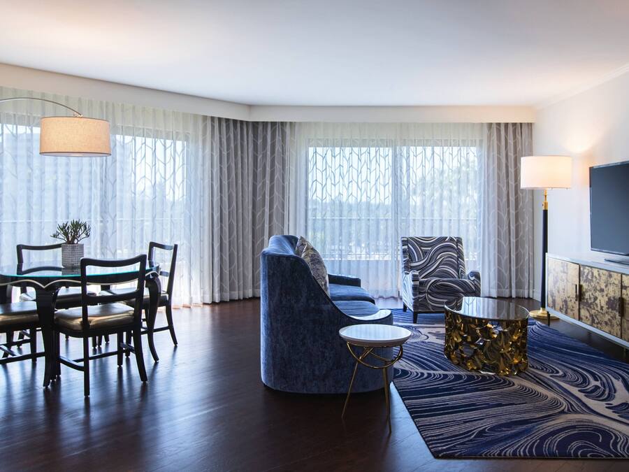 Una sala de estar moderna con sofá, sillón, mesa de comedor, sillas, televisor y una alfombra estampada.
