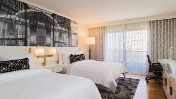 A hotel room with two beds, a desk, a chair, a lamp, and a large abstract painting on the wall.