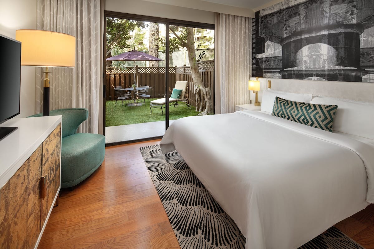 A hotel room with a bed, a TV, a desk, and a view of the outdoor patio.