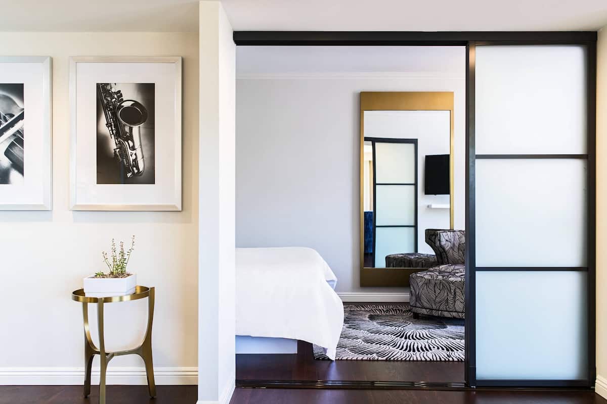 A hotel room with a bed, a chair, a small table with a plant, and framed pictures on the wall.