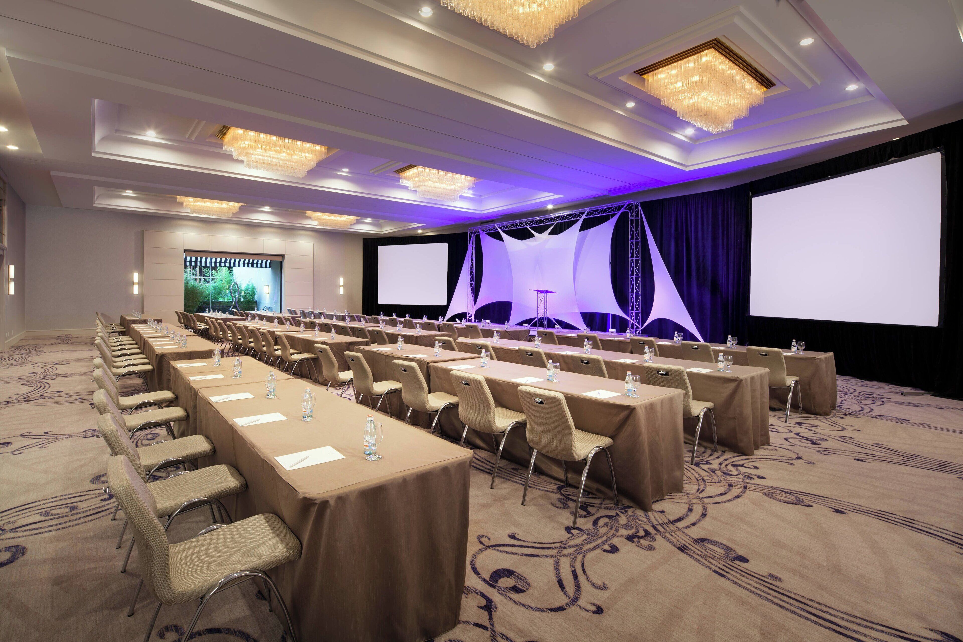 A conference room with long tables, chairs, and a large screen.