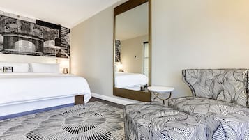 Hotellihuone, jossa on sänky, suuri peili, kuviollinen nojatuoli ja pieni pöytä.
