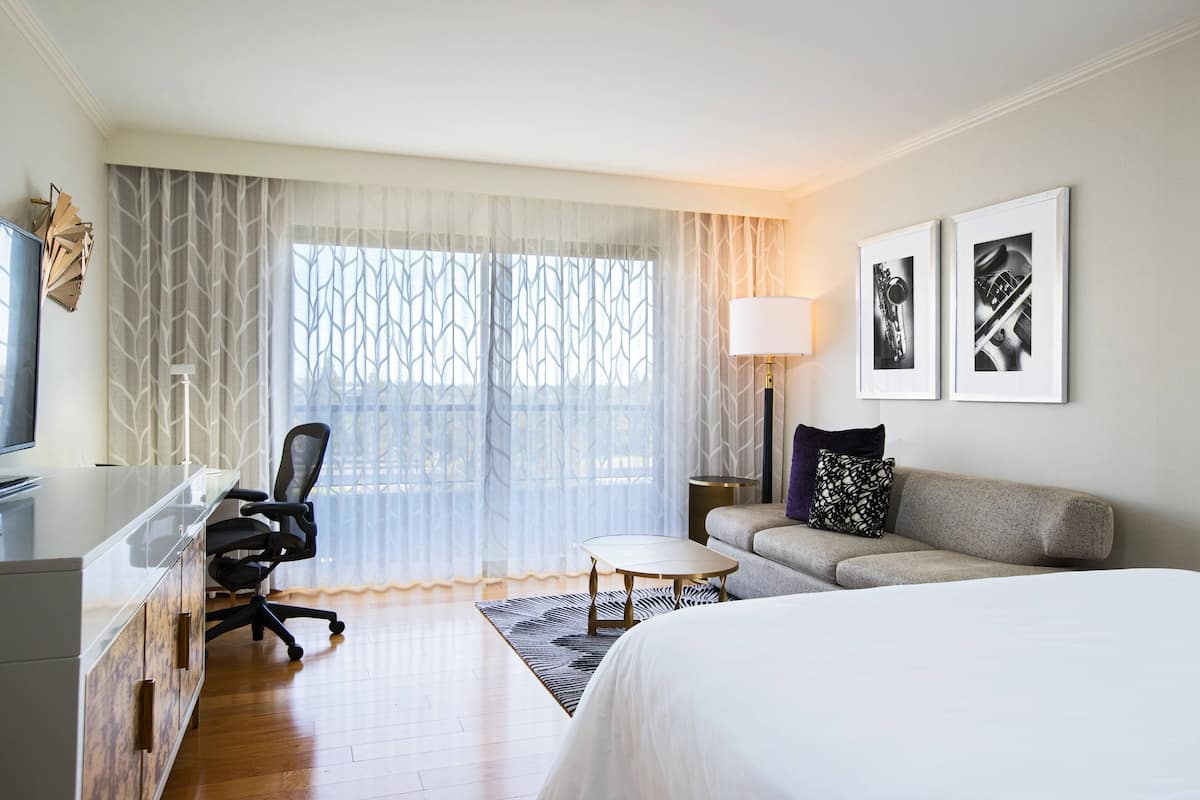 A hotel room with a bed, a desk, a chair, a sofa, a lamp, and two framed pictures on the wall.